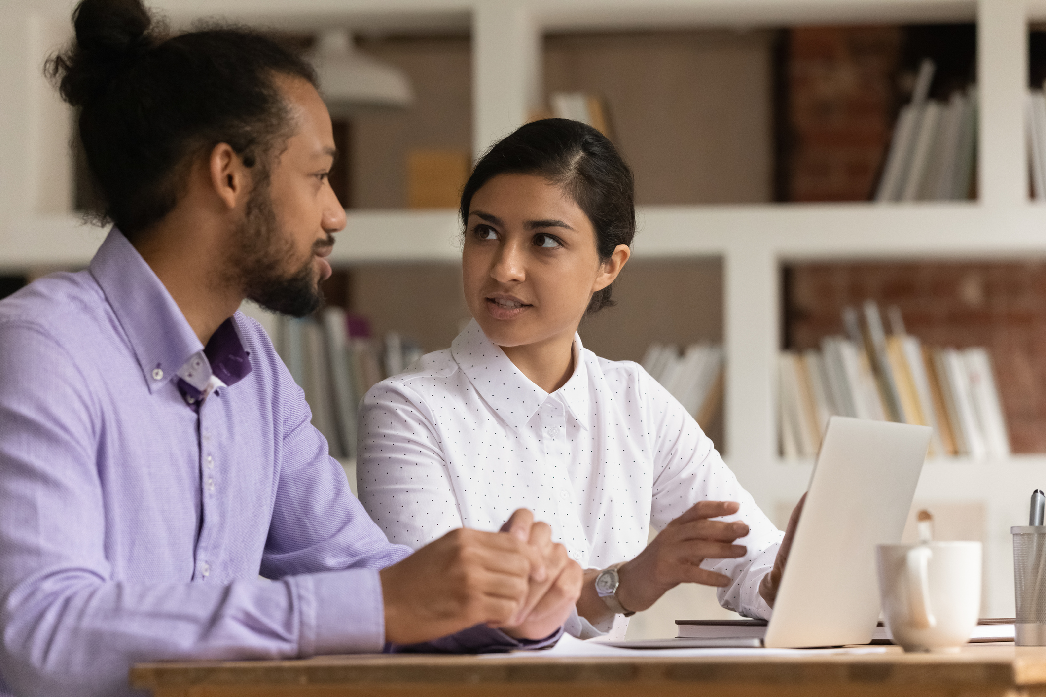 Photo of multiethnic colleagues sit at desk communicating discuss current business