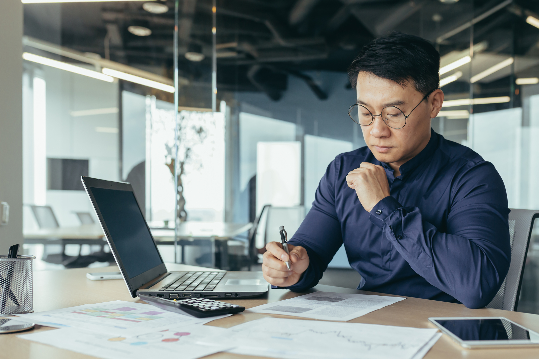 Photo of a male sitting at a desk in an office setting thinking with a computer and paperwork.